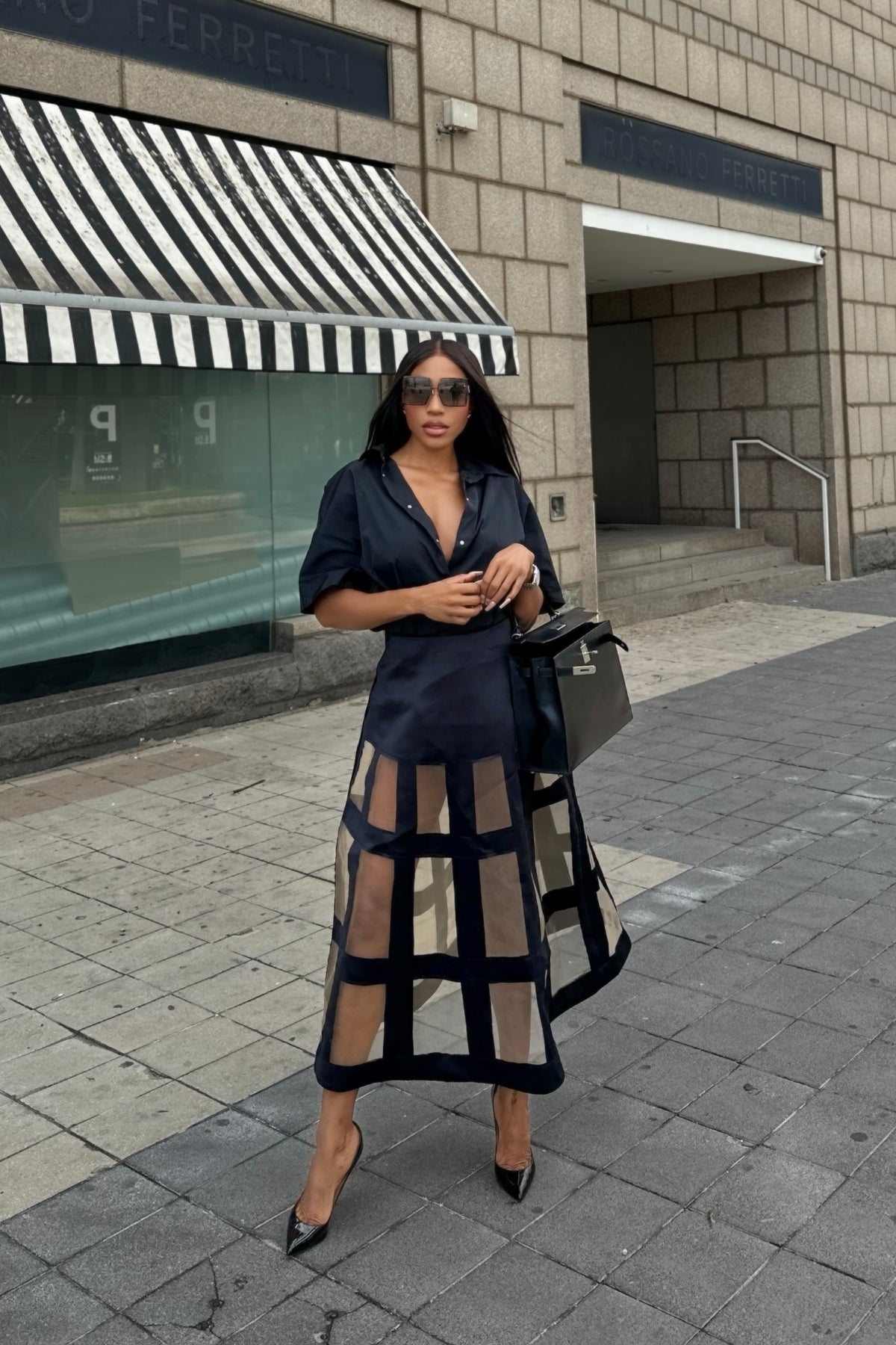 Woman in a black dress with sheer panels standing on a city street.