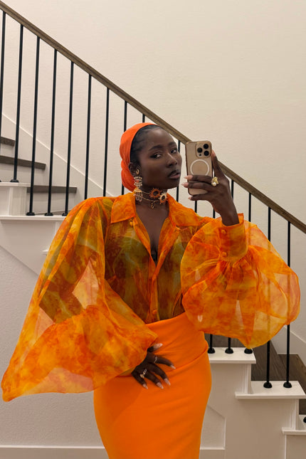 Person wearing an orange outfit taking a mirror selfie in a staircase.