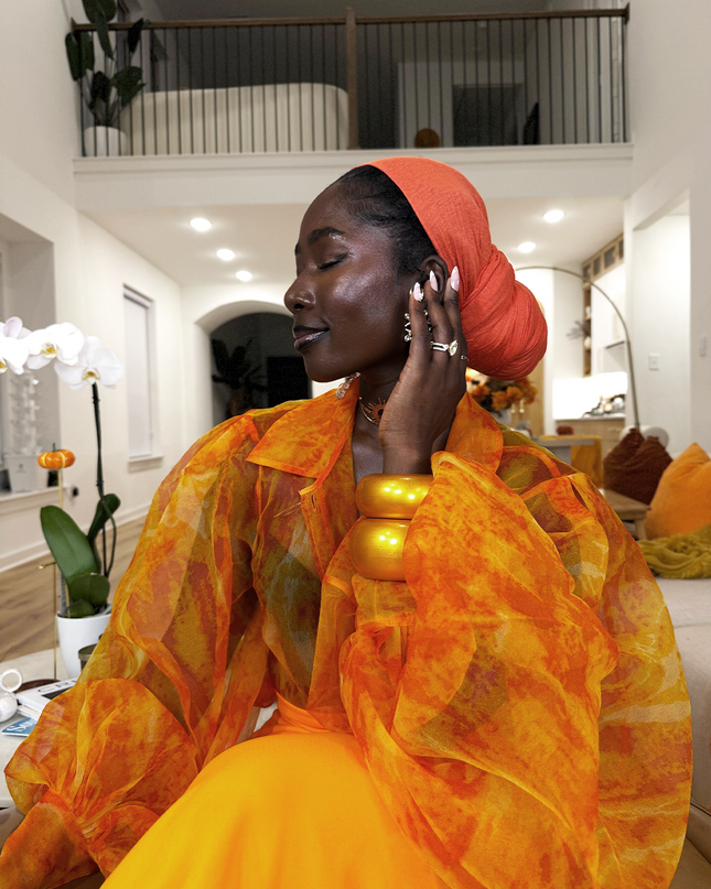 Woman in an orange and yellow outfit with a red headscarf in a modern indoor setting.