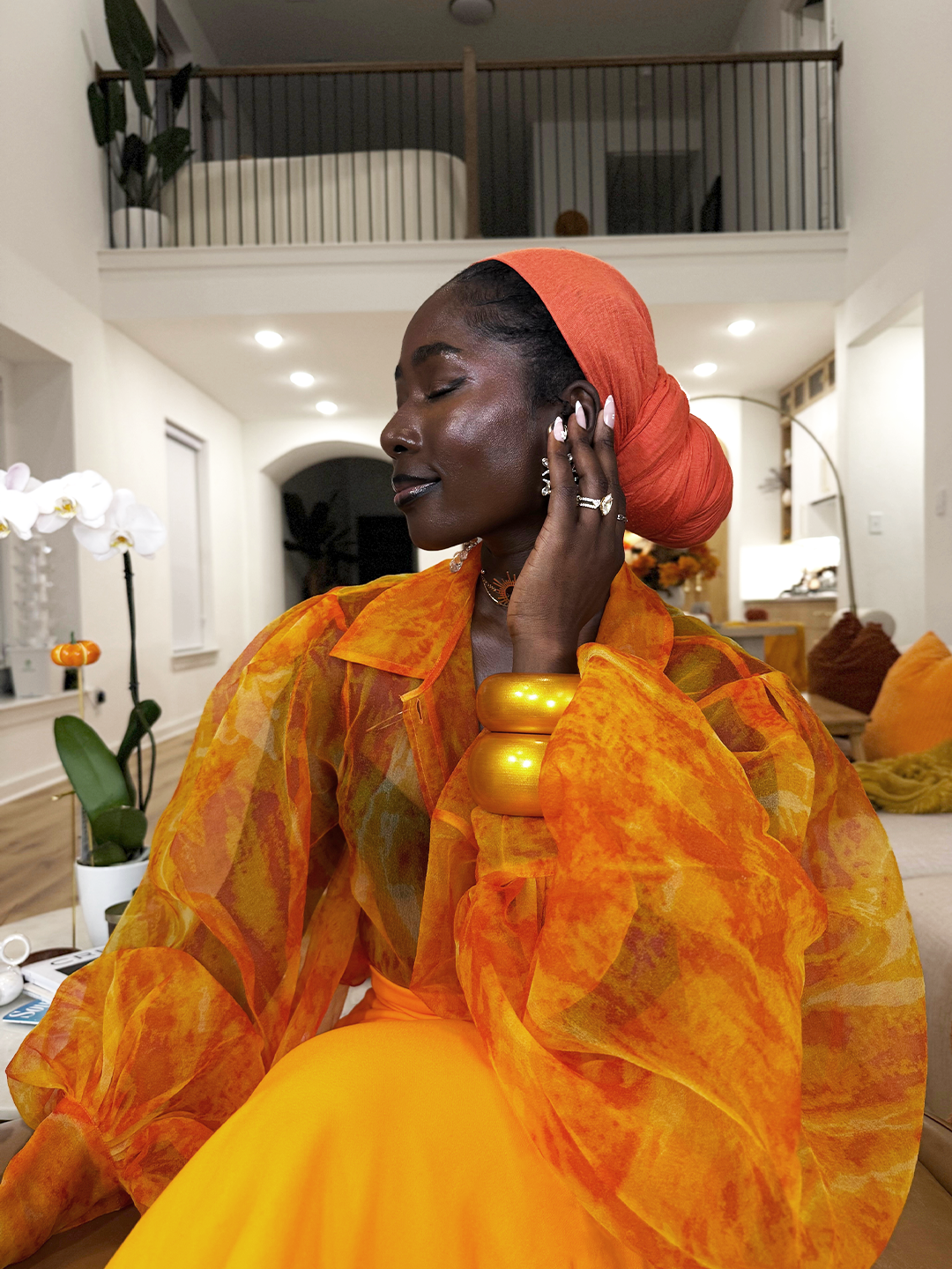Woman in an orange and yellow outfit with a red headscarf in a modern indoor setting.