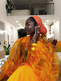 Woman in an orange and yellow outfit with a red headscarf in a modern indoor setting.