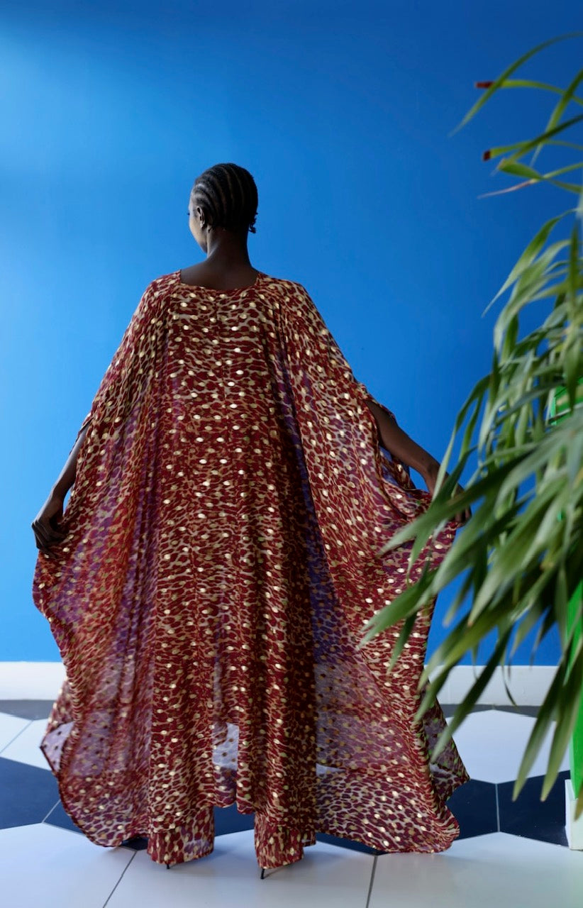 The Afet Pants feature a ruby red and beige cheetah print pattern. The sheer fabric allows its wearer to get creative with how they style the pants.