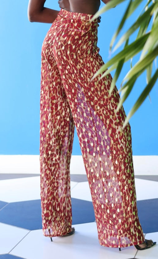 The Afet Pants feature a ruby red and beige cheetah print pattern. The pants are specked with gold touches as well as warm brown detailing.