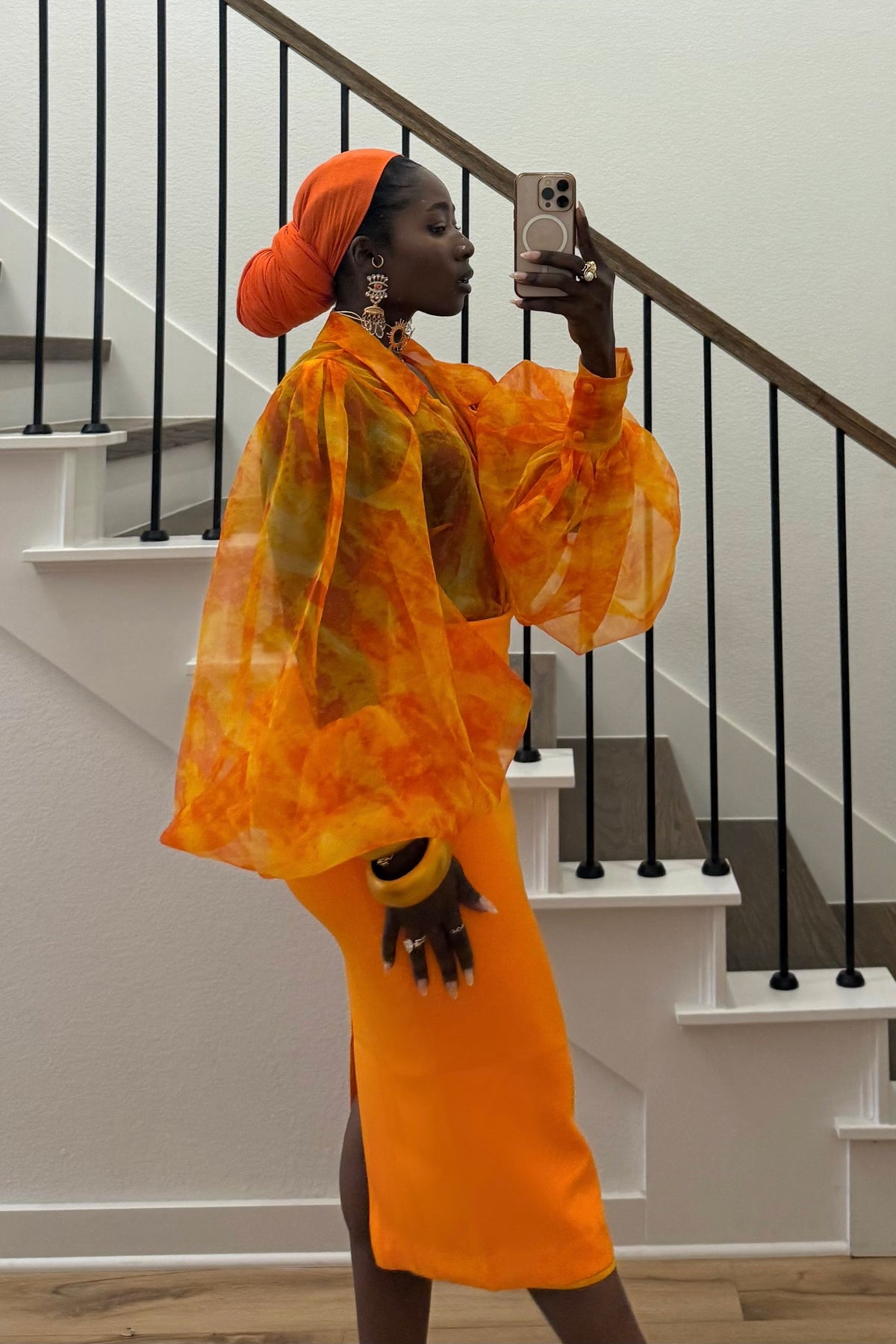 Person in an orange outfit taking a selfie in front of a staircase.